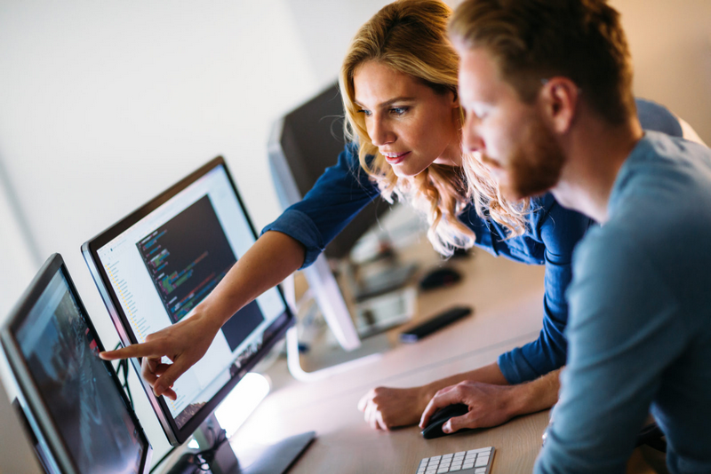 Two people work together on a computer, with one pointing at the screen.