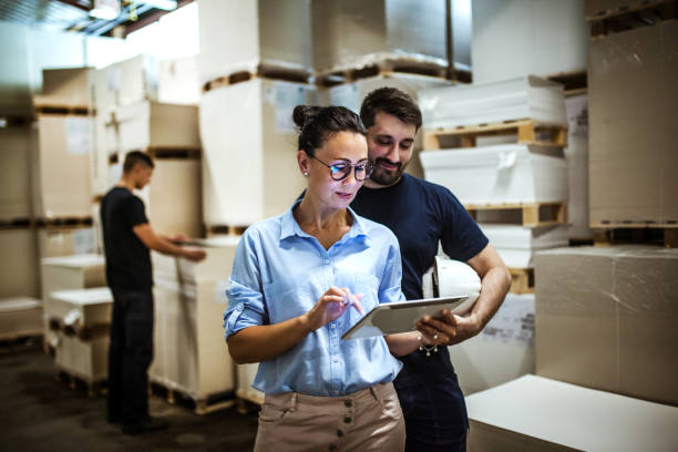 Two colleagues review a budget on a tablet in a warehouse.