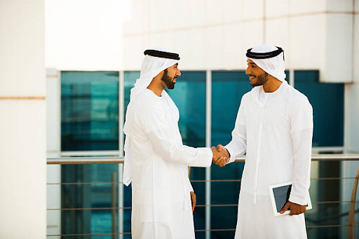 Two entrepreneurs in traditional attire handshake, discussing opportunities in the IFZA Free Zone.